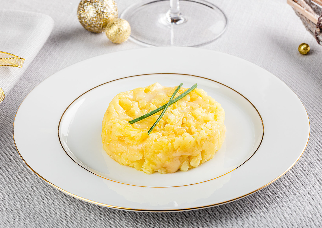 Une écrasée de pommes de terre au Comté AGIS, de couleur jaune, présentée dans une assiette blanche et agrémentée de quelques brins de ciboulette